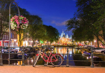 Fotobehang met rode fiets op een Amsterdams bruggetje bij avond, omringd door verlichte grachtenpanden en stille grachten.