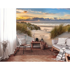 Een woonkamer met een fotobehang met de duinen bij de Noordzee met een uitgestrekt strand en een schitterende zonsondergang, met warme kleuren.