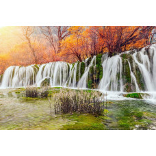 Fotobehang van een waterval die door een herfstlandschap stroomt, met kleurrijke bomen en bladeren eromheen.