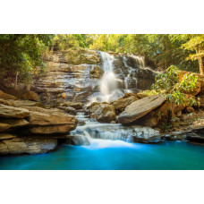 Fotobehang van een zonnige waterval die door rotsen stroomt, met een helderblauwe lucht en een stralende zon.